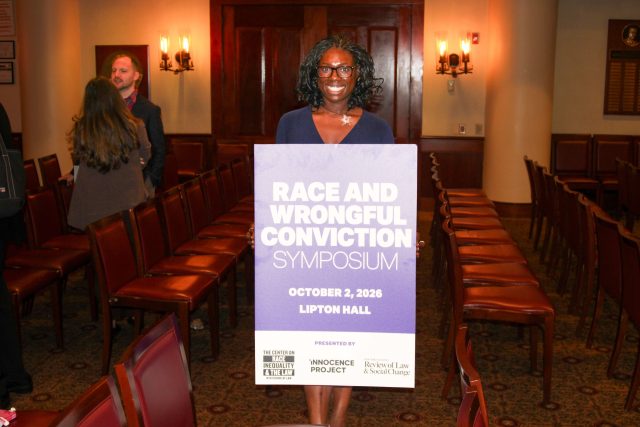 An attendee holds up a poster for the event with the words "Race and Wrongful Conviction Symposium, October 2, 2026, Lipton Hall."